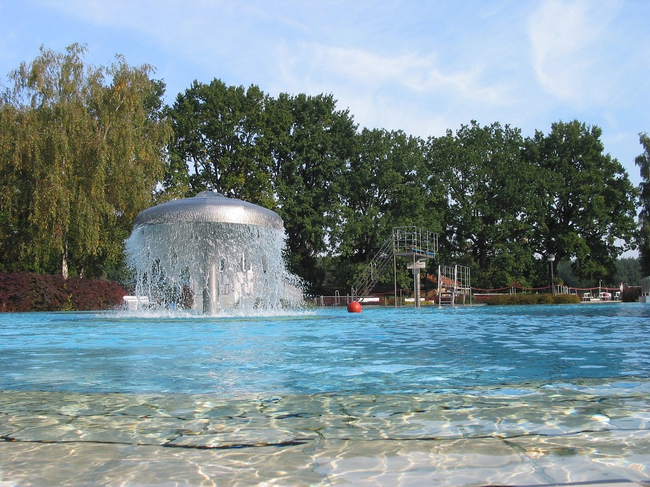 Freibad mit Wasserattraktion und Bäumen im Hintergrund